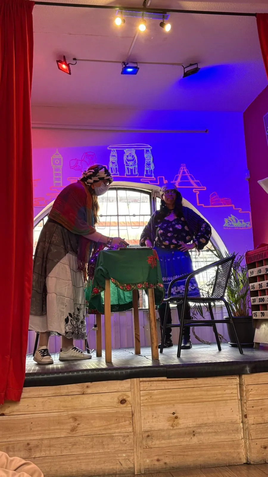 Dos alumnas representan una escena sobre el escenario, con vestuario y luces de colores
