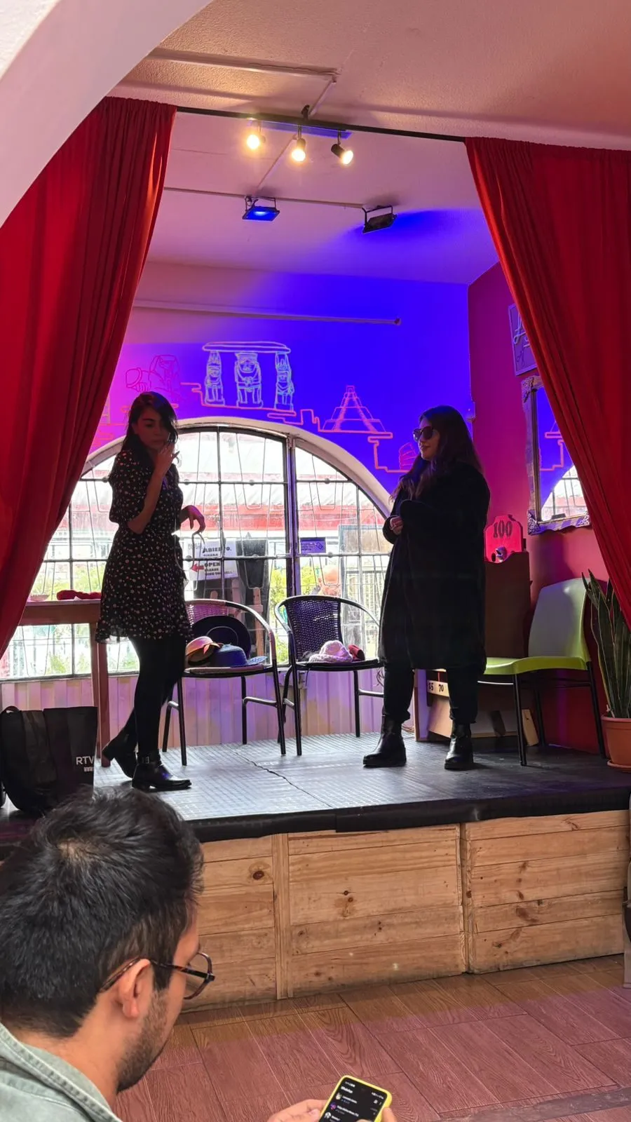 Escena en la que dos personajes conversan junto a una mesa, con la luz azul del fondo
